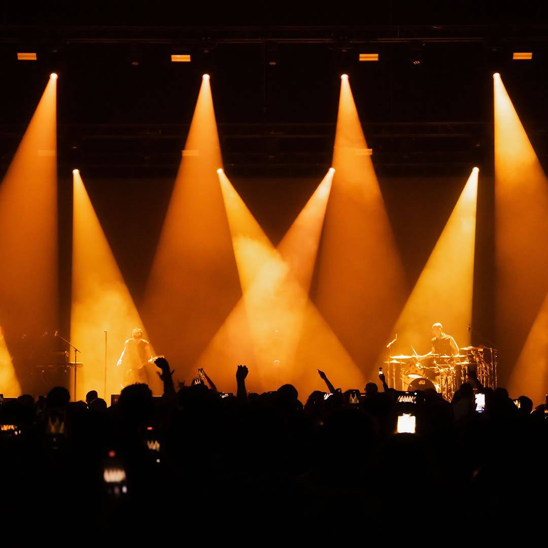 Concert stage and audience framed by dramatic amber spotlights