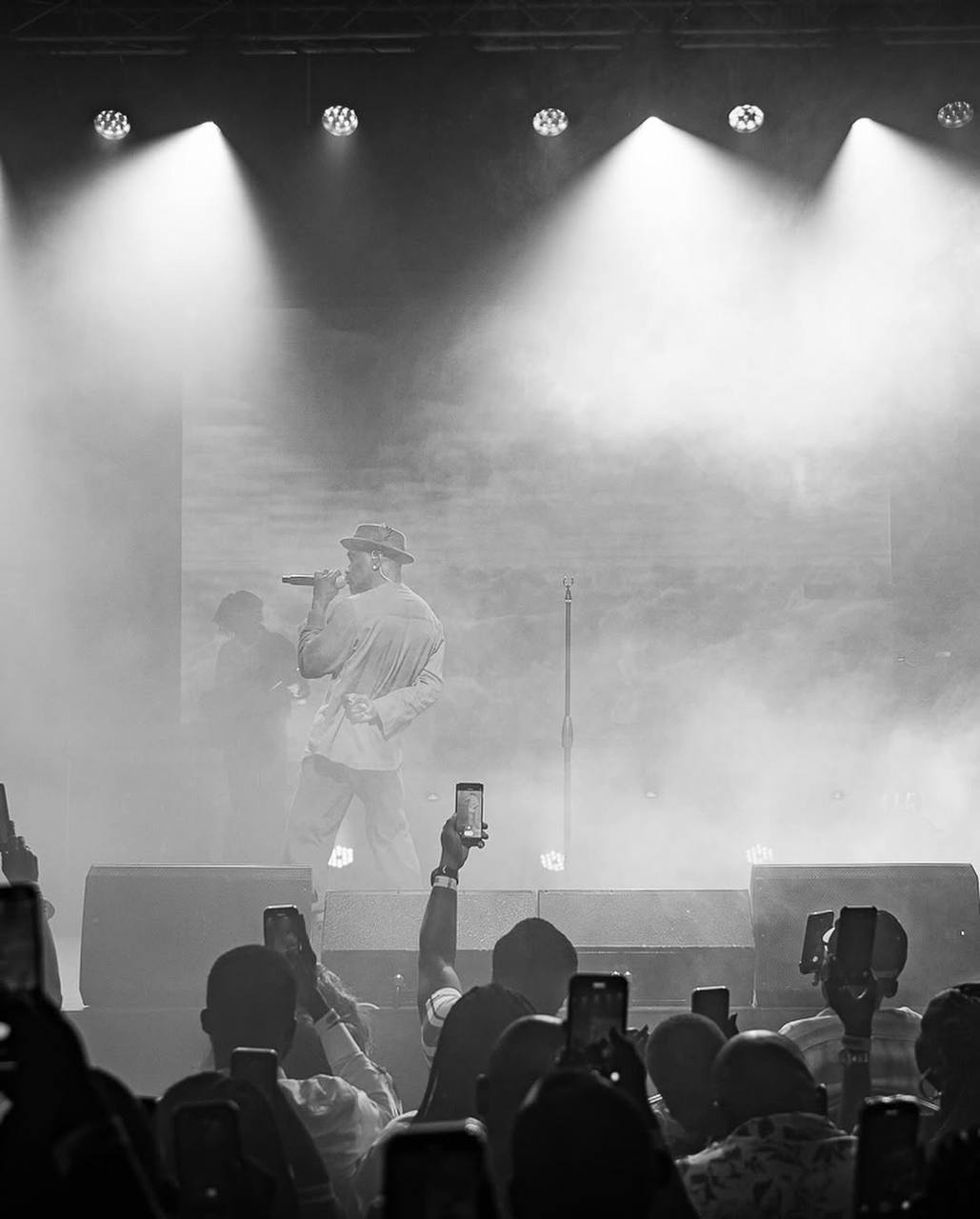 Monochrome live performance beneath white spotlights with the audience in the foreground