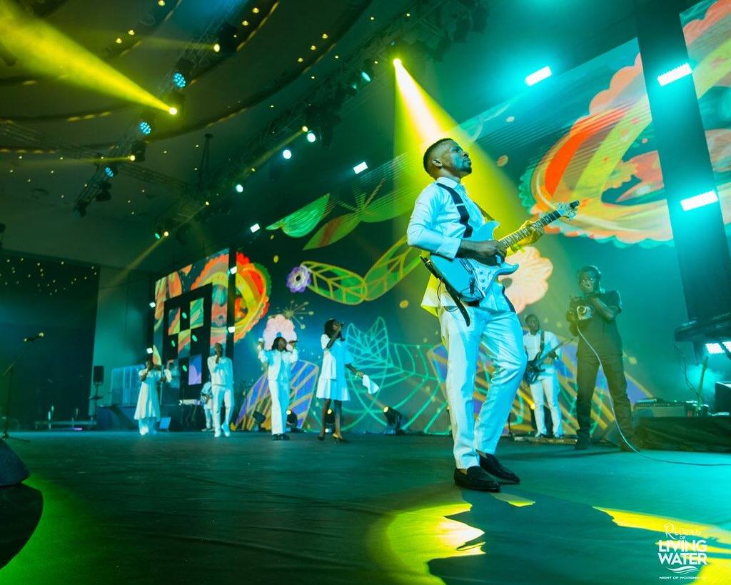 Guitarist performing on a green-lit stage with colorful LED visuals