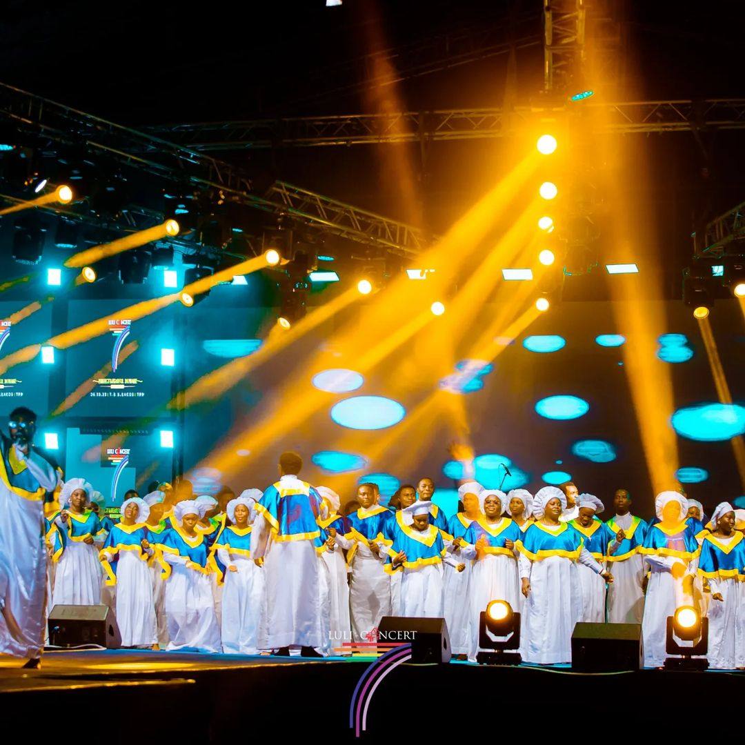Large choir performing beneath warm gold beams on a concert stage