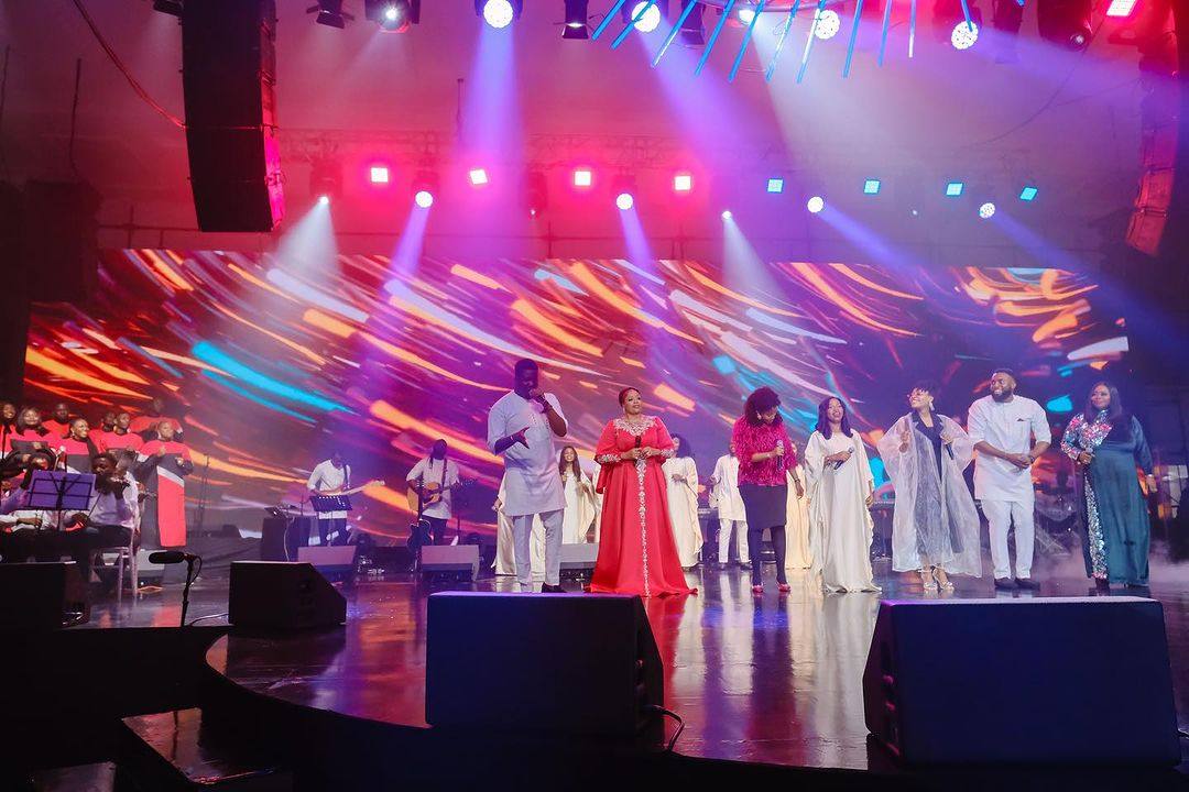 Worship team and choir performing on a wide stage beneath colorful lighting and a vivid LED backdrop